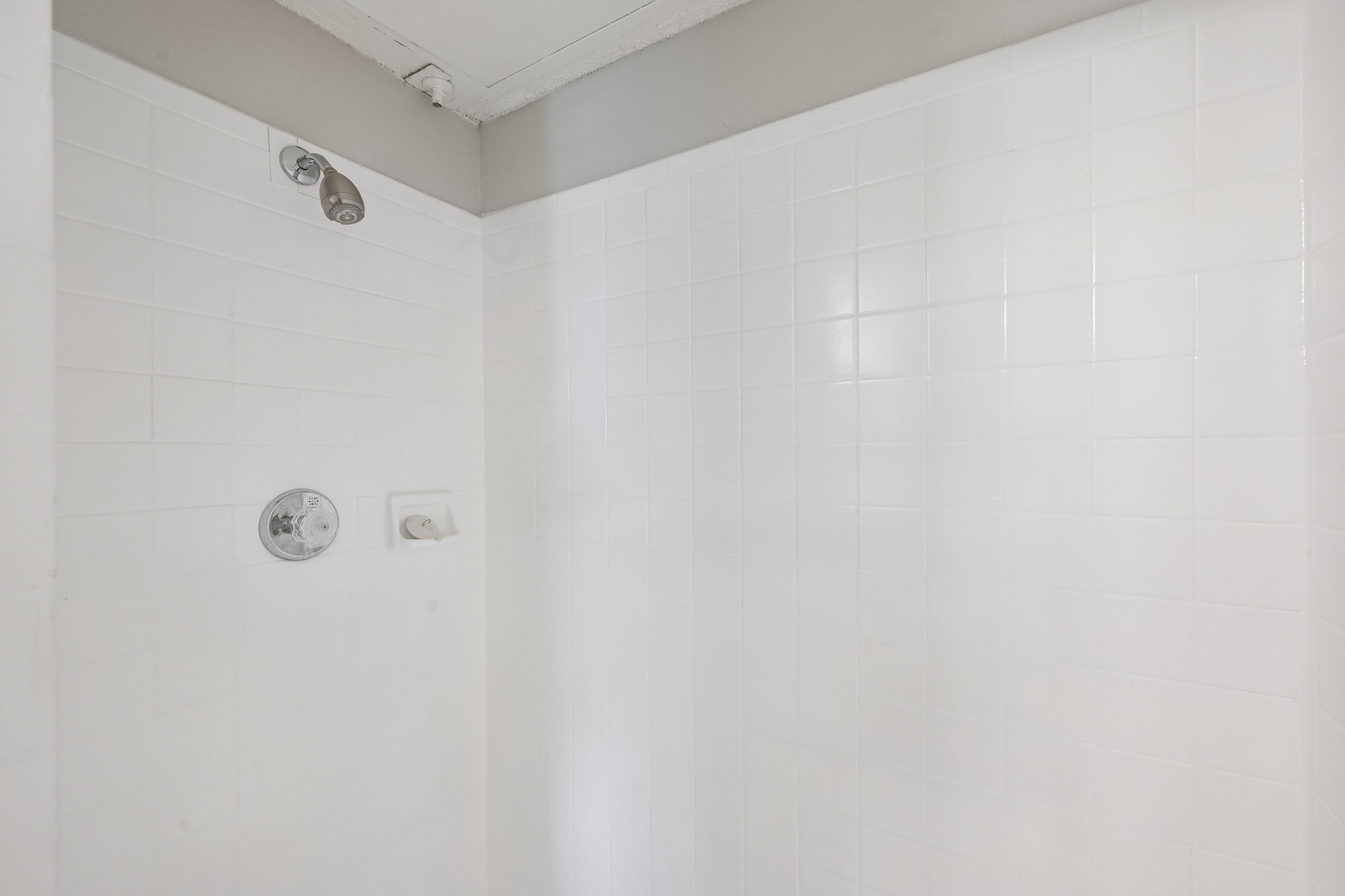 A white tiled shower with a shower head and a faucet.